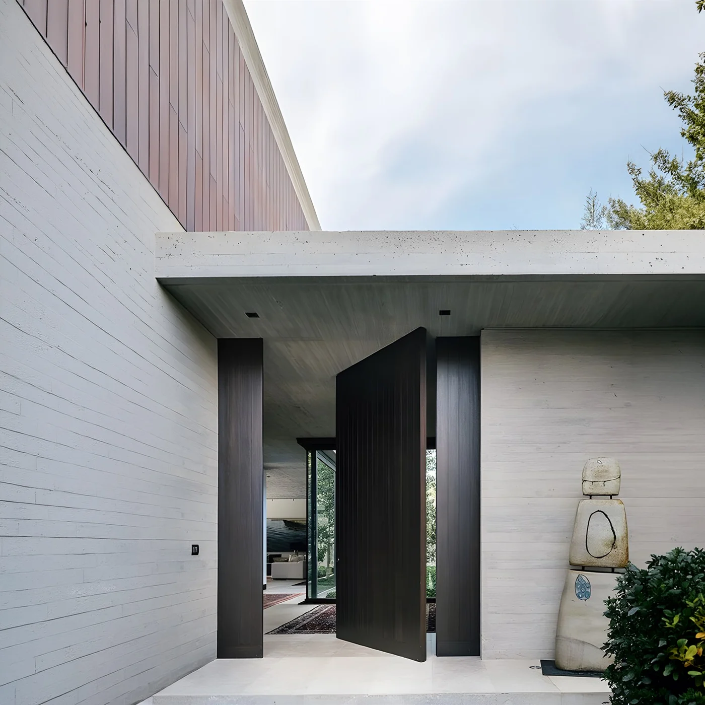 Dark aluminium pivot entrance door with a long handle in a light architectural facade